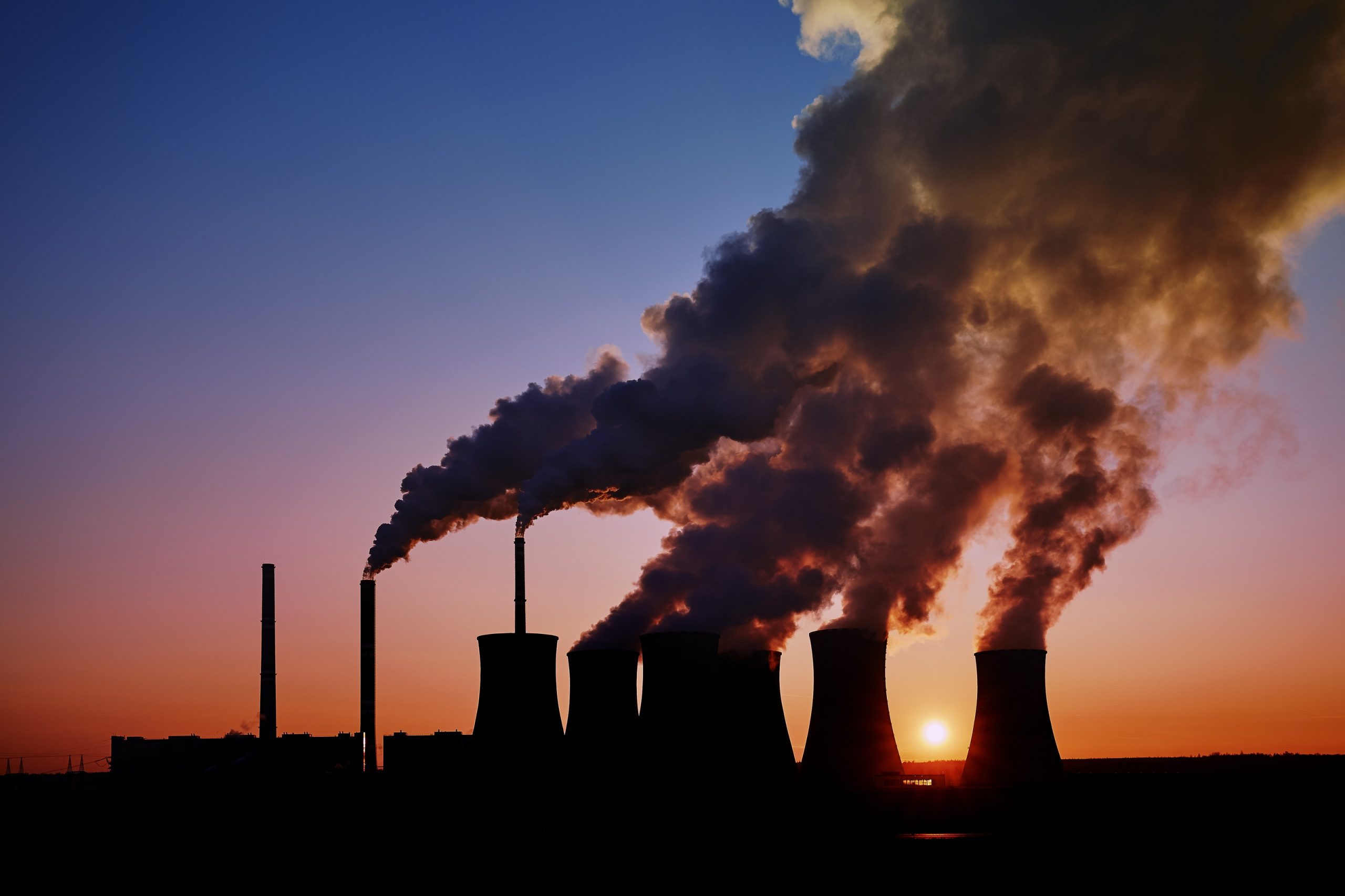 smoke is coming out of the cooling towers of a power plant during sunset